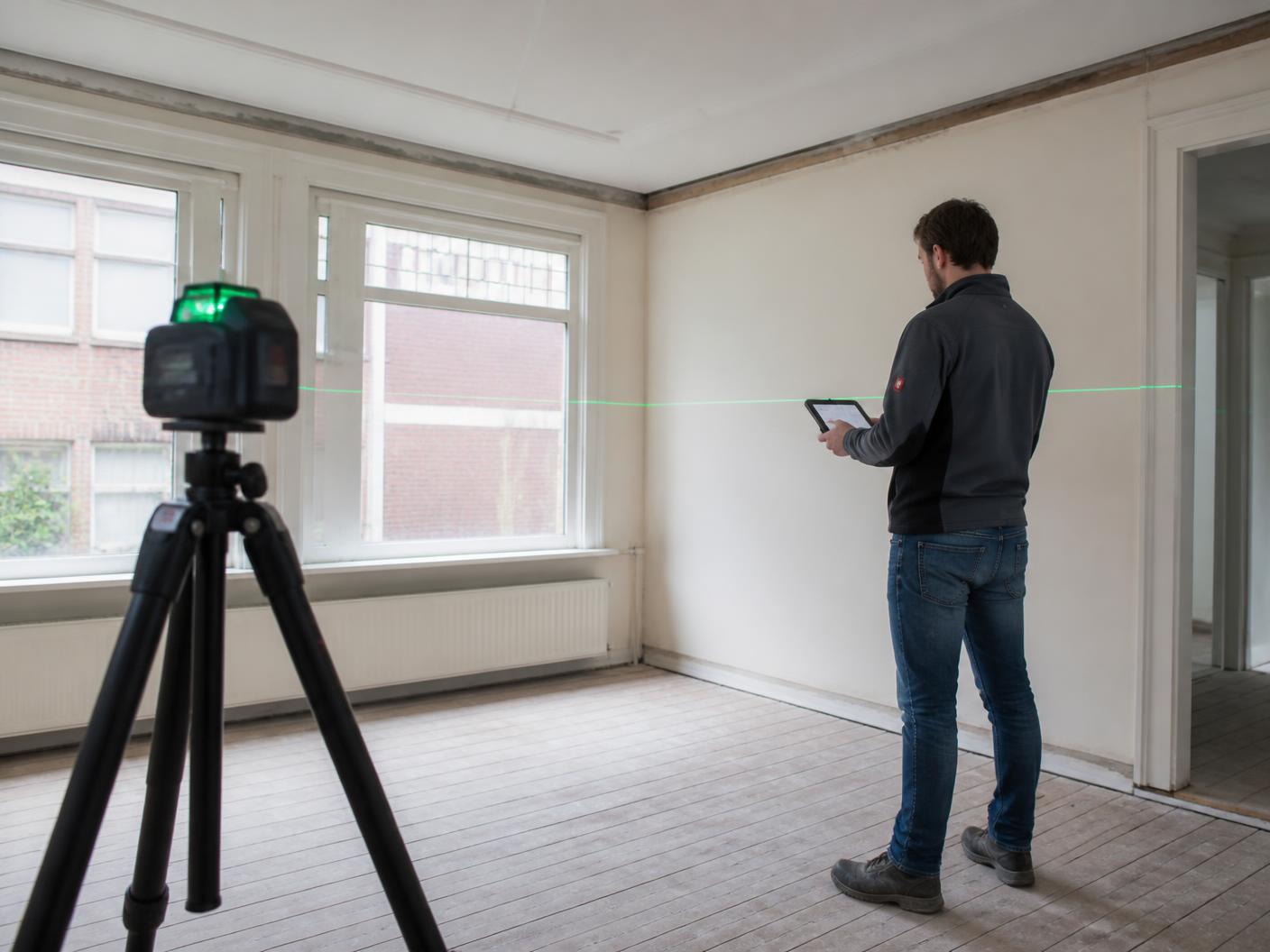 Bouwkundige meet met een lasermeter de bestaande situatie van een woning in